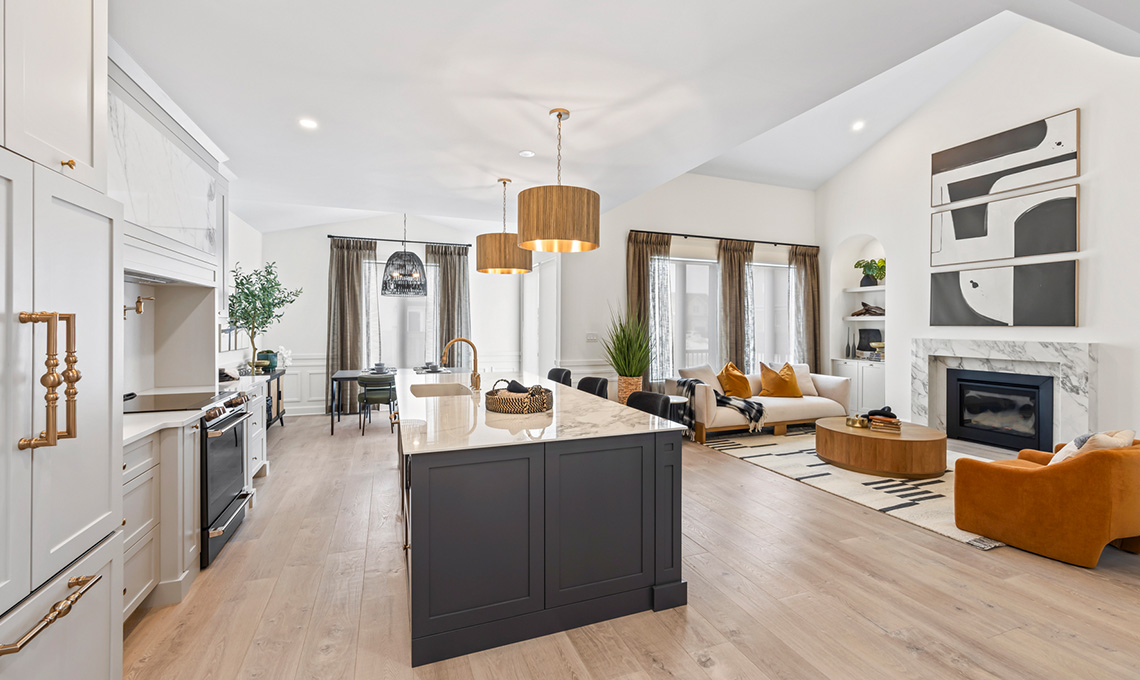 An open-concept room with a kitchen on one side and sofas near a fireplace on the other side.