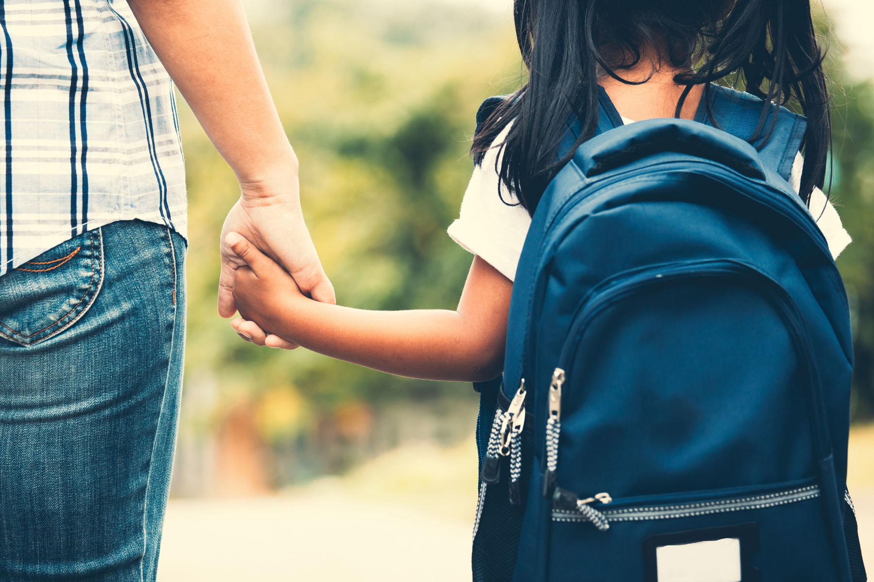 A mother hold's her daughter's hand as they walk to school.