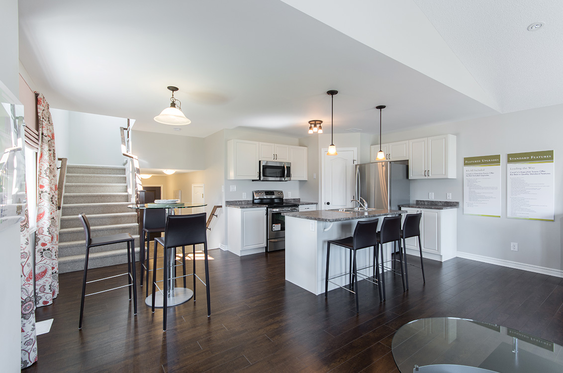 A bright kitchen with dark wood floors stands beside stairs going both up and down.
